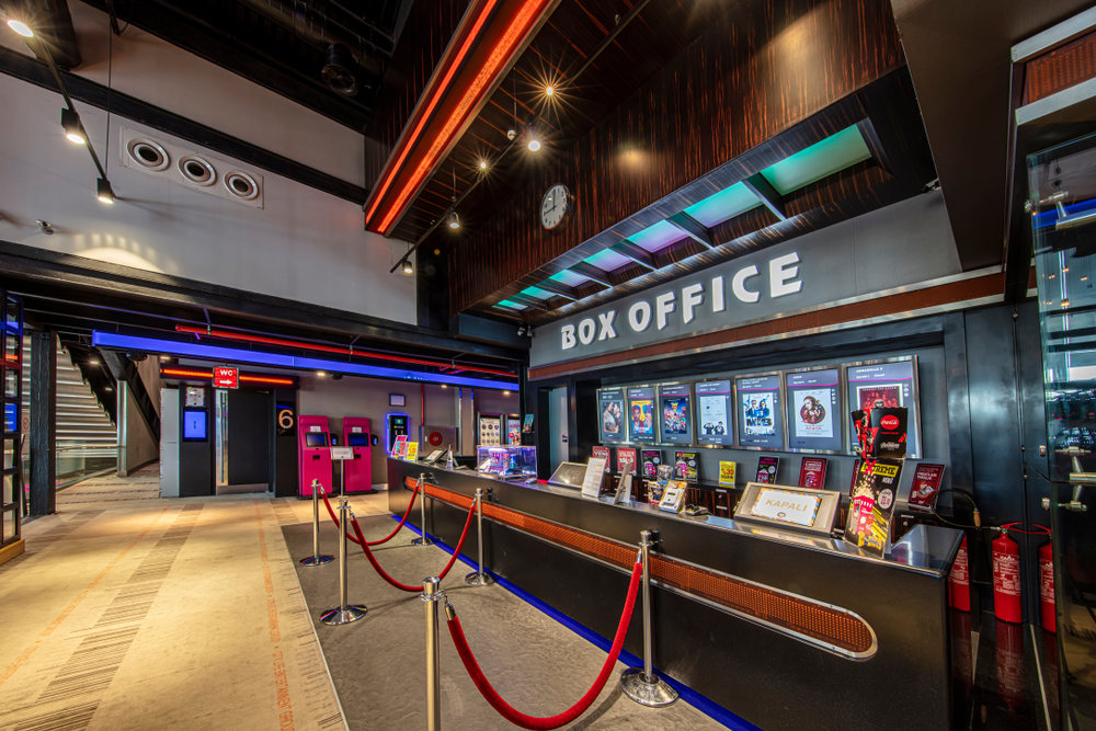 The box office and lobby of a modern cinema, with self-service kiosks, film posters, and a queue barrier